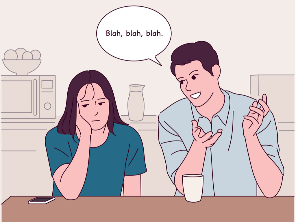 Man and woman sitting in kitchen with the man talking and woman resting her head in her palm while glancing at her phone.